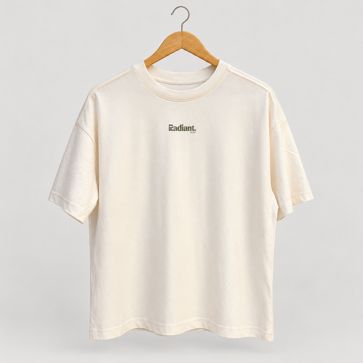 Front of cream oversized Radiant Pilates T-shirt on wooden hanger with small olive chest logo